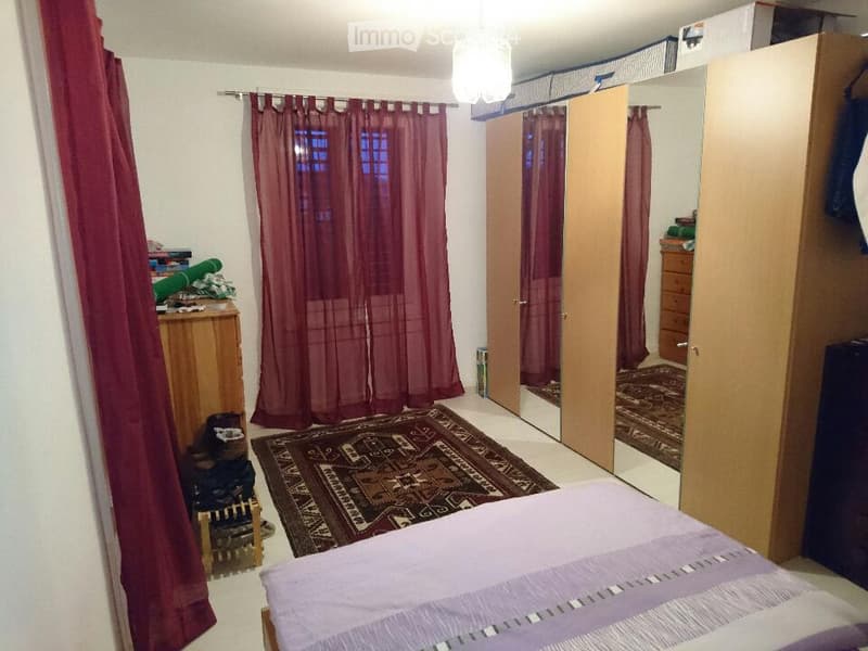 Cozy bedroom with a bed, wooden wardrobe, dresser, purple curtains, and a patterned rug.