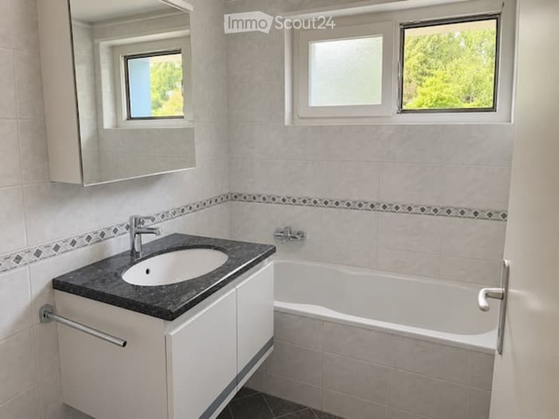 Modern bathroom with a white bathtub, a black countertop sink, a mirror cabinet, and a window with a view of greenery.