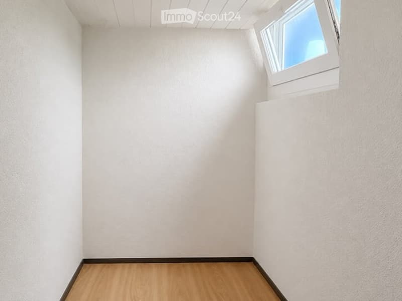 Completely empty room with light-colored walls and wooden flooring, featuring a single window with white frame and blinds.