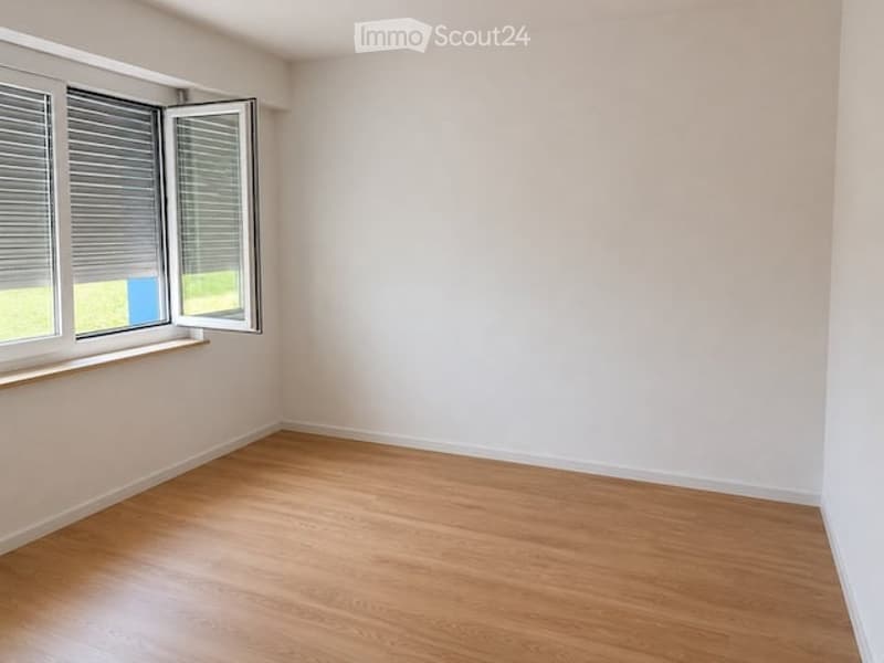 Empty room with light wooden flooring, white walls, and large windows with blinds. No furniture or equipment present.