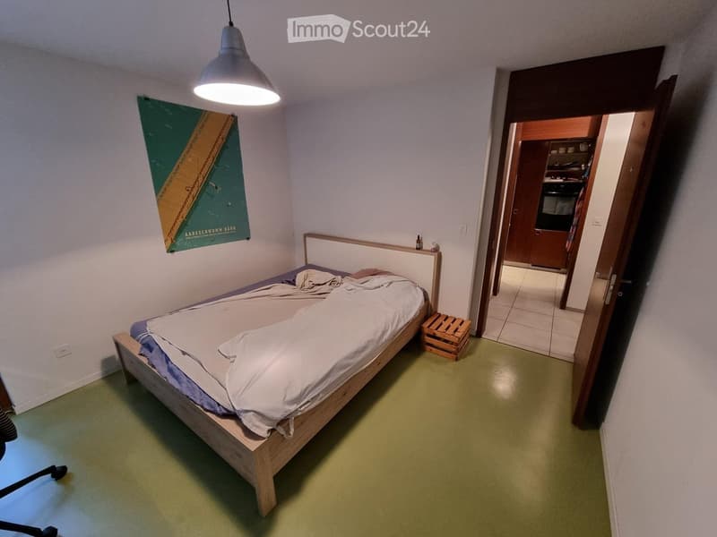 Bedroom with a wooden bed, pendant light, poster on wall, and small wooden stool near the bed.