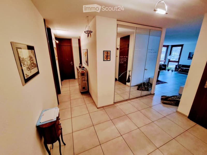 Hallway with tiled floor, white walls, and several doors leading to different rooms. A small table with papers and a framed map is visible on the left, and a mirror is mounted on the wall near the end of the hallway.