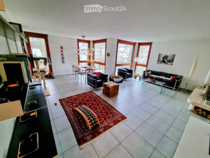 Bright living room with large windows, tiled floor, red rug, sofa, coffee table, cat tree, dining table, and chairs.