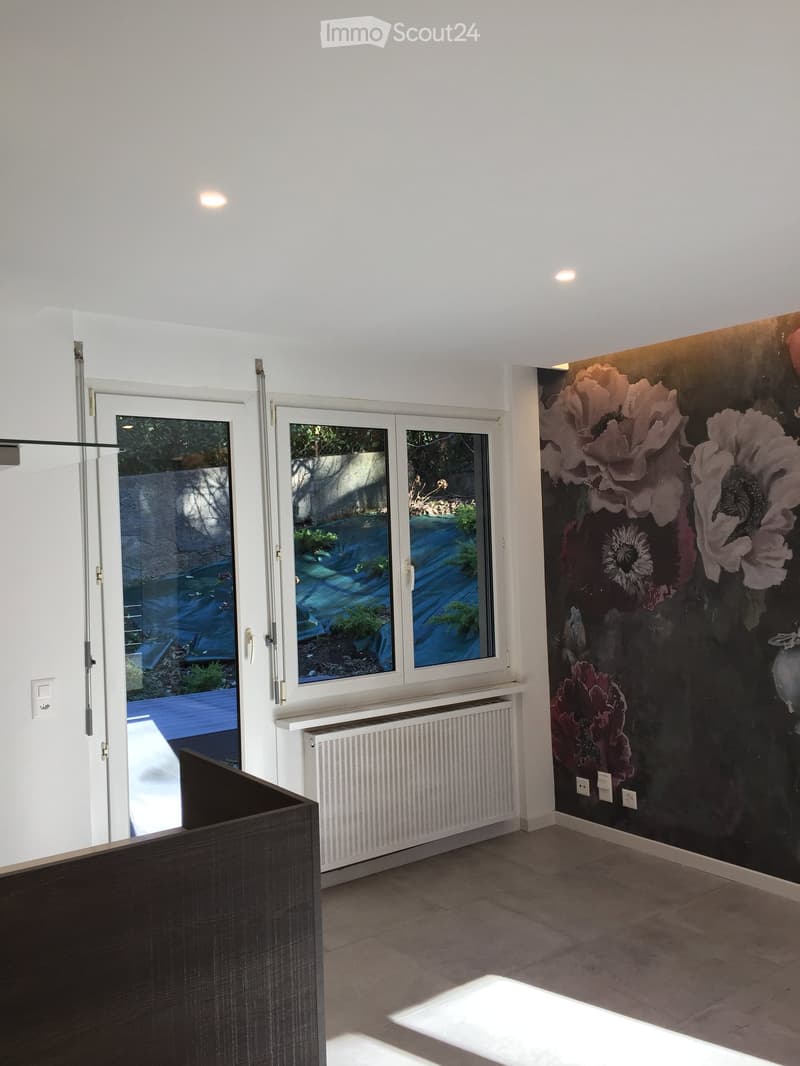 Empty room with white walls, large windows, radiator, and a floral wallpaper mural on one wall.