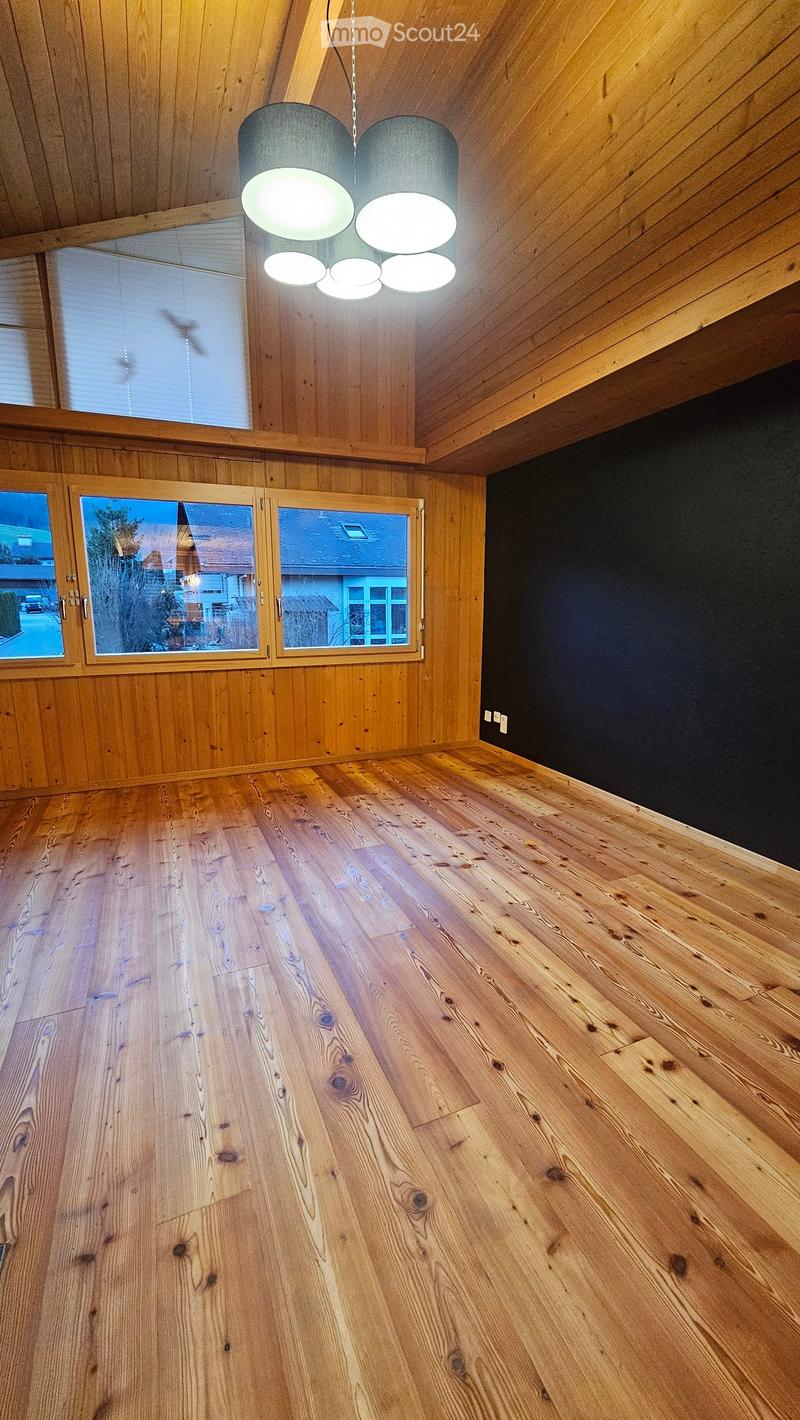 Empty room with wooden flooring, wooden walls, large windows, and a modern hanging light fixture.