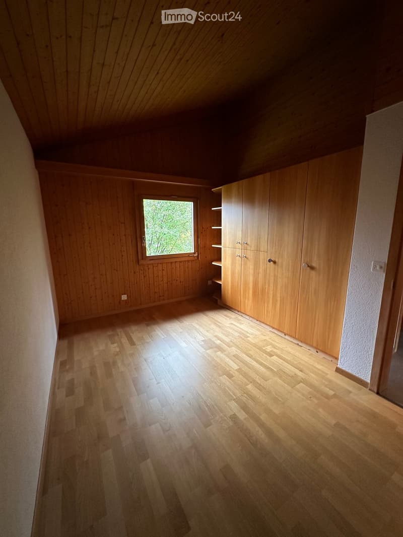 Empty room with wooden walls, wooden floor, built-in wooden cabinets, and a window letting in natural light.