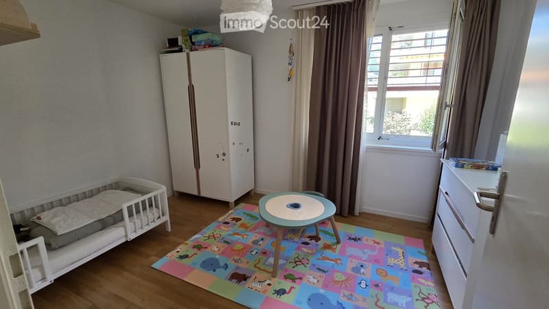 Child's bedroom with a crib, small table, colorful rug, and wardrobe.