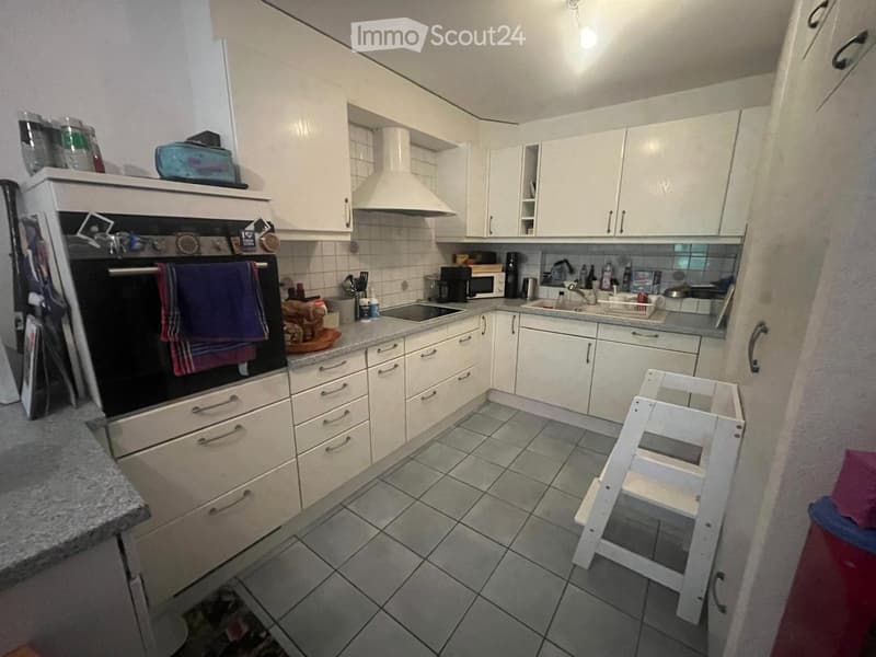 A compact kitchen with white cabinets, a tiled floor, and various appliances including an oven, microwave, and sink.
