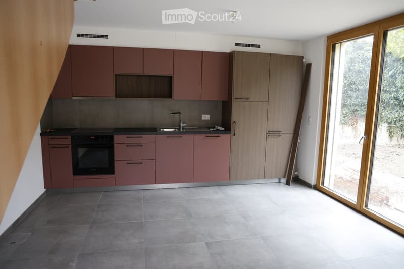 Modern kitchen with maroon cabinets, white countertops, gray tiles, black stove, and a stainless steel sink.