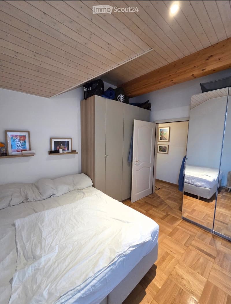 Cozy bedroom with a single bed, white bedding, a wardrobe, a large mirror, and a shelf with picture frames and decorative items.