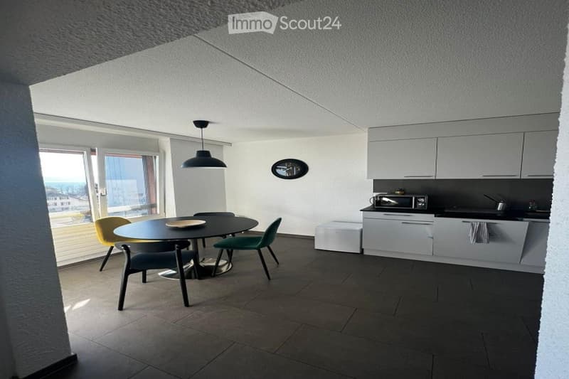 Modern kitchen and dining area with white cabinets, a round black dining table with four chairs, a microwave, and a view through large windows.