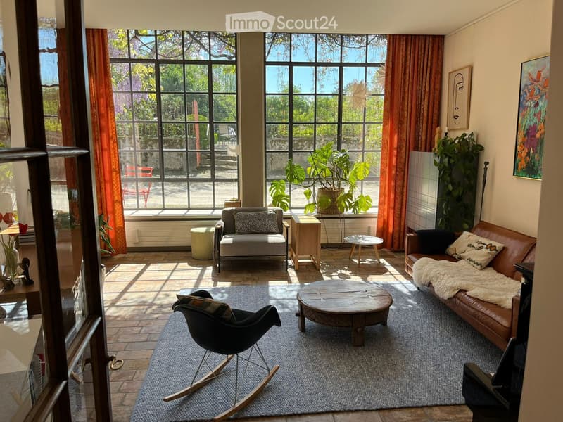 Living Room. Bright living room with large windows, leather sofa, coffee table, armchair, and plants.