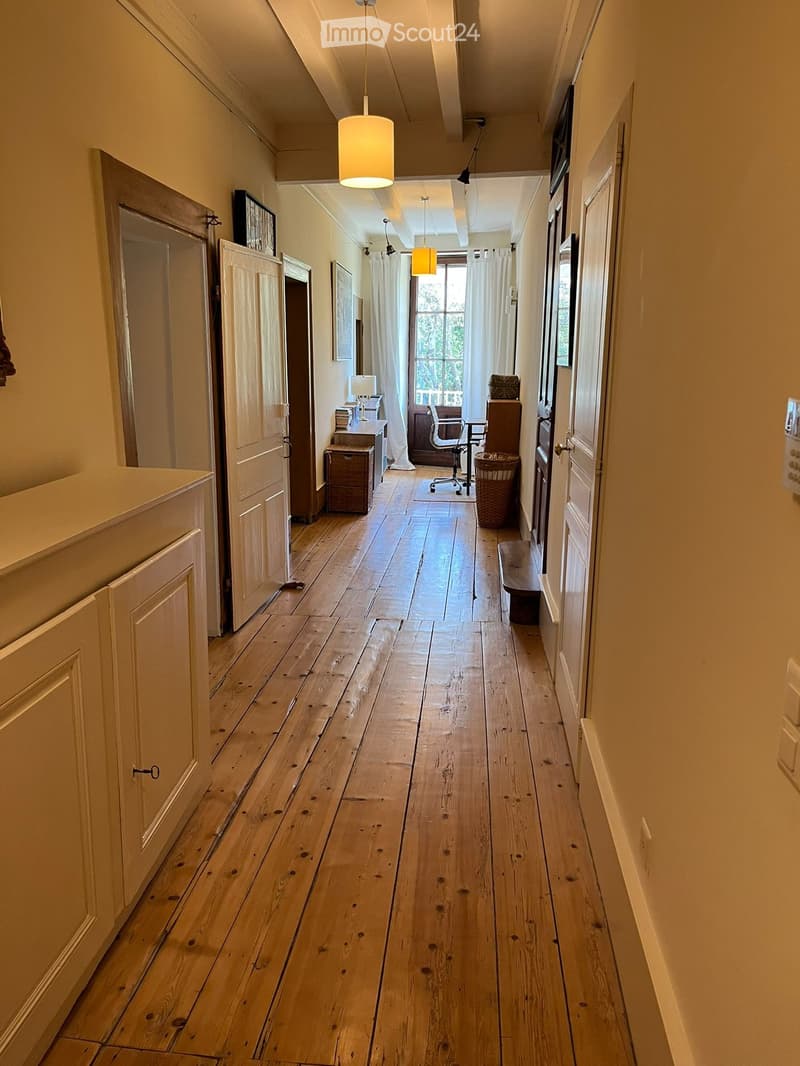 Corridor / Hallway. Long wooden hallway with multiple doors, pendant lights, and a small seating area at the end.