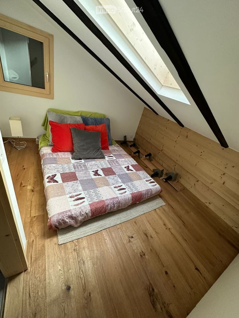 Cozy attic bedroom with wooden floors, slanted ceilings, and a small bed with colorful pillows and a patterned quilt.