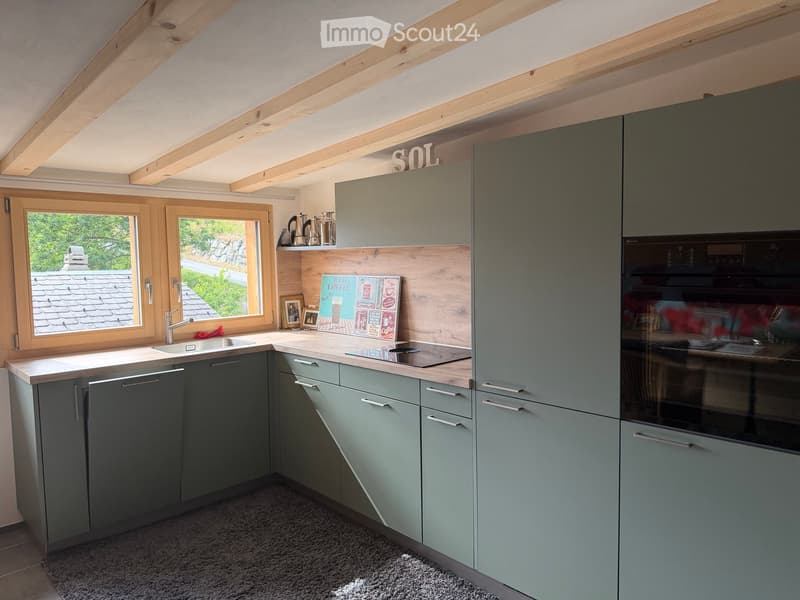 Modern kitchen with grey cabinets, wooden countertops, and stainless steel appliances. Features a sink, oven, and coffee maker on the counter.