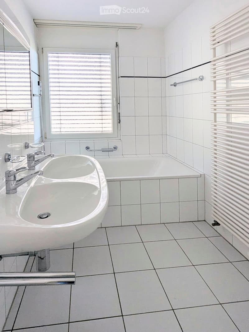 Modern bathroom with white tiles, a sink with a modern faucet, a bathtub, and a radiator on the wall.