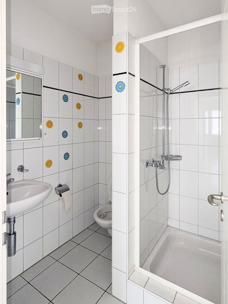 Bathroom with white tiles, a sink, toilet, bathtub, and shower. Features a glass shower enclosure and a mirror with decorative tiles.