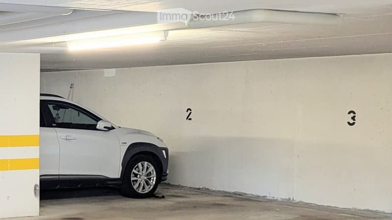 Underground parking area with a white SUV parked inside, marked spaces numbered 2 and 3, concrete walls and ceiling with fluorescent lighting.