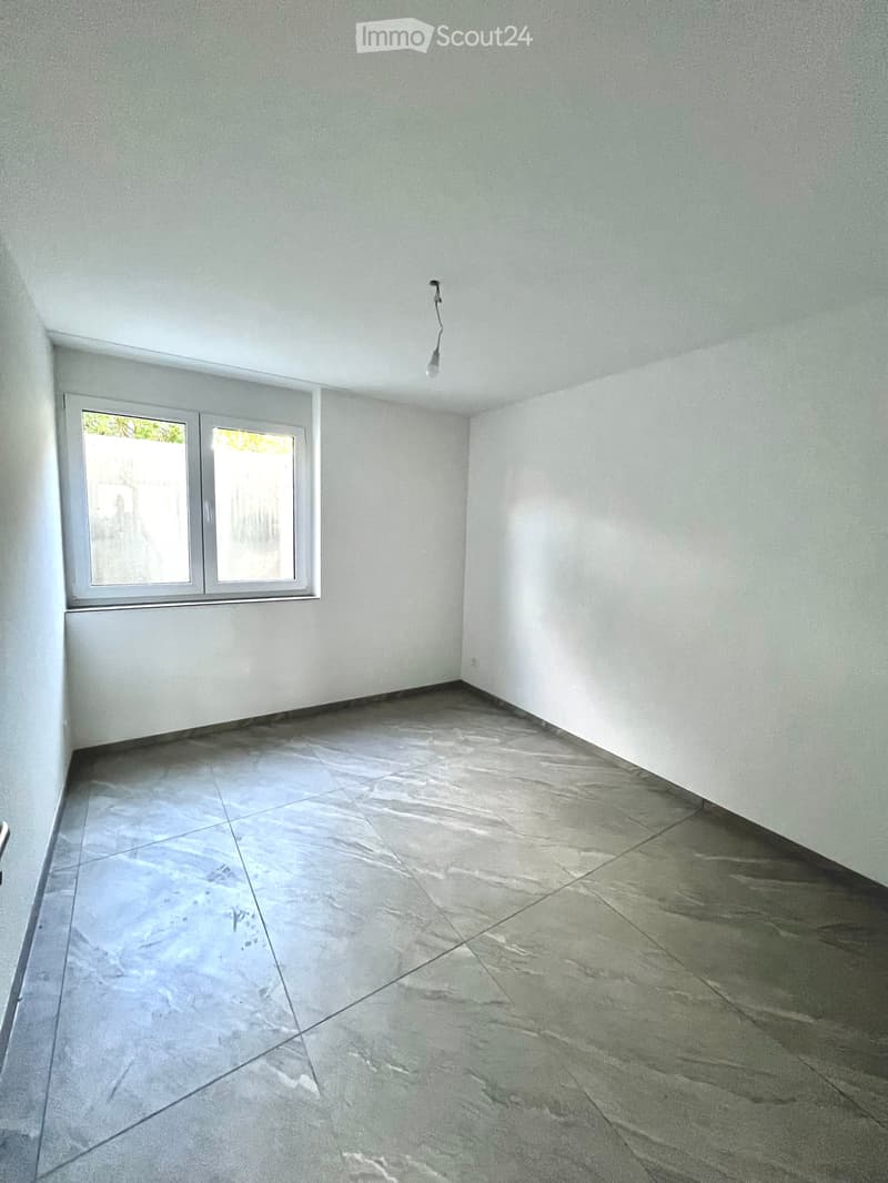 Empty room with light grey tiled floor and white walls, featuring a single window with frosted glass and a single light fixture on the ceiling.
