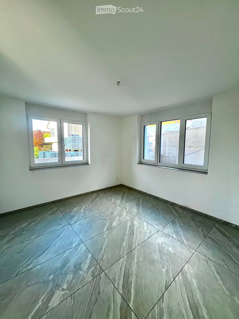 Empty room with light grey tiled floor and white walls, featuring multiple windows with metal frames and blinds.