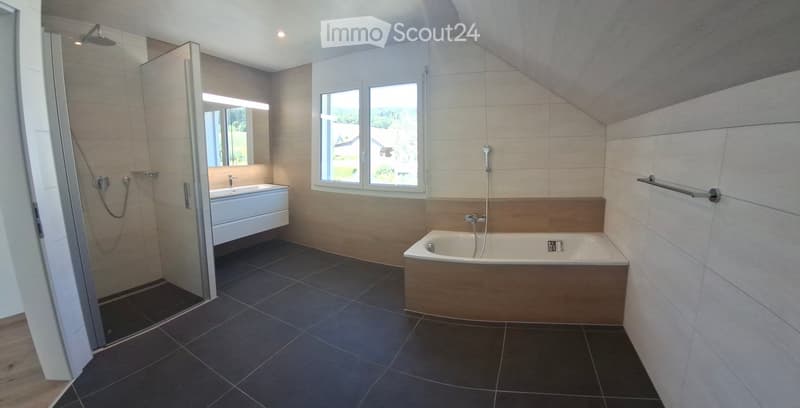 Modern bathroom with a bathtub, sink, and walk-in shower. Features large windows, dark tiled flooring, and a sleek design.