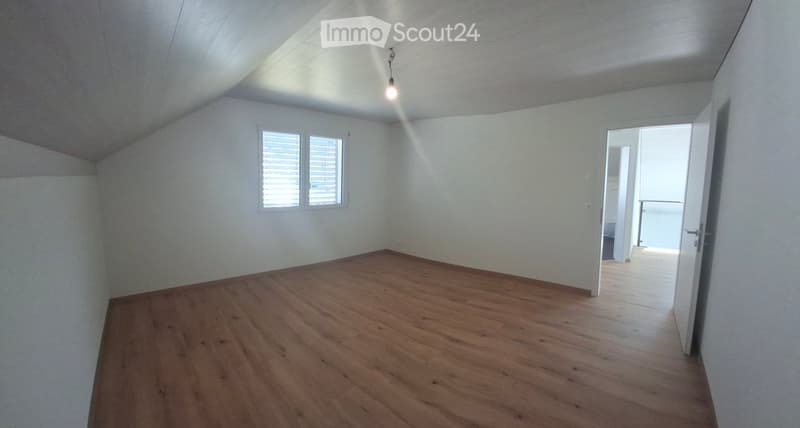 Empty room with wooden flooring, white walls, and a window with blinds. A doorway leads to another space.