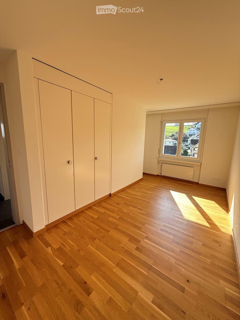 Empty room with light wooden flooring, white walls, built-in closet, and a window with a view of the outside.