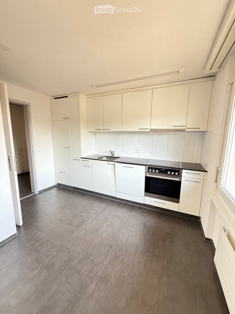 Modern kitchen with white cabinets, a sink, and an oven, featuring a tiled backsplash and wooden flooring.