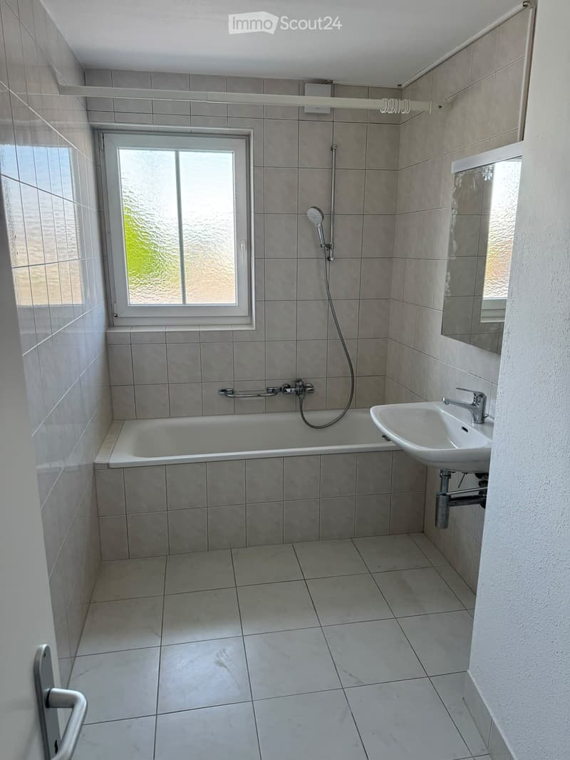 Modern bathroom with tiled walls and floor, featuring a bathtub, sink, mirror, and showerhead.