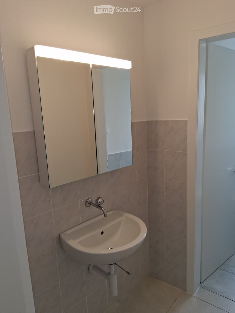 Modern bathroom with a white sink, chrome faucet, built-in mirror with LED lighting, and tiled walls.