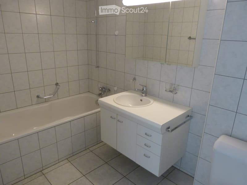 Bathroom with a bathtub, sink, and cabinet. The walls are tiled, and there is a mirror above the sink.