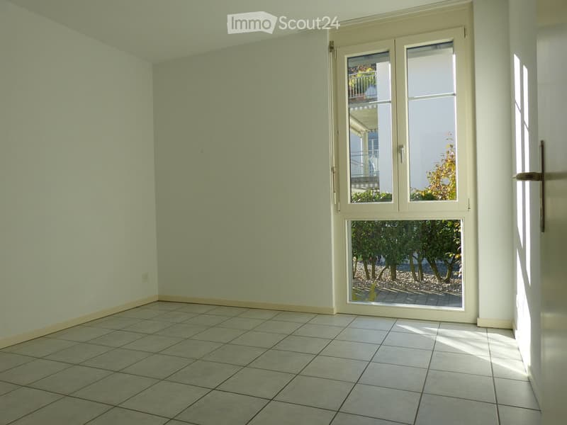 Empty room with tiled floor, light green walls, and a large sliding glass door leading to an outdoor area with trees and a paved patio.