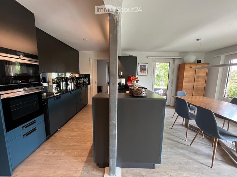 Modern kitchen with dark blue cabinets, stainless steel appliances, island, and dining area with wooden table and blue chairs.