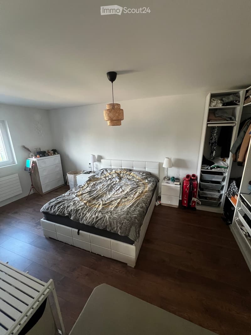A modern bedroom with a large bed, white headboard, nightstands, lamps, a wardrobe, and a small desk area with a screen and chair.
