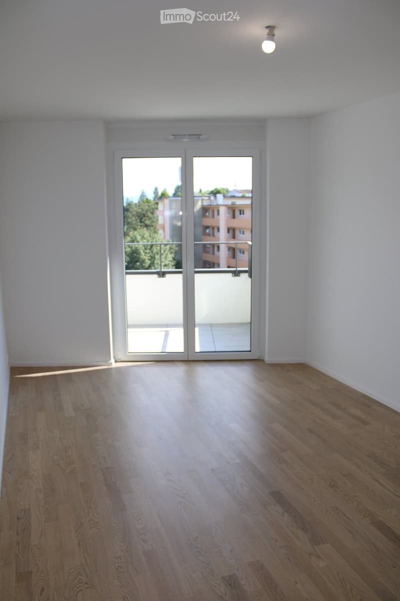 Empty room with light wooden flooring, white walls, and a large glass door leading to a balcony.