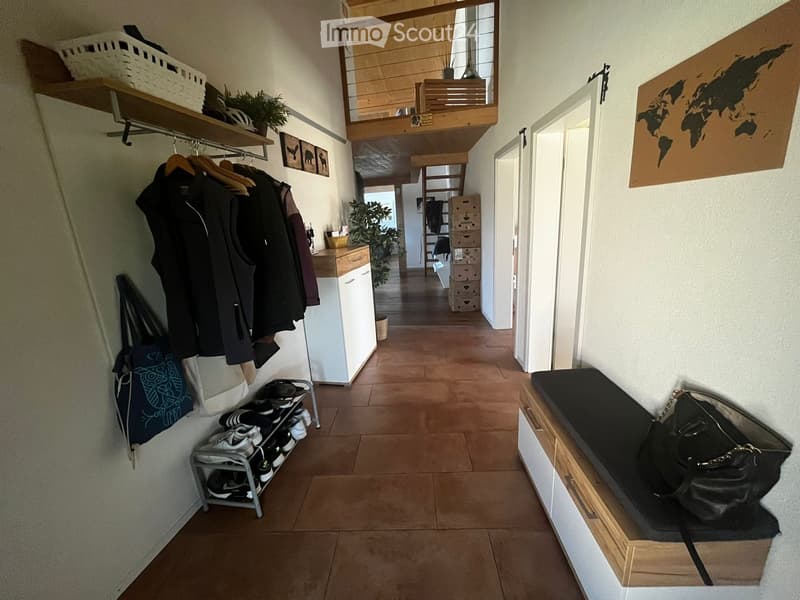 Well-lit hallway with tiled floor, coat rack, shoe shelf, and storage bench. Features a world map poster and a small plant in the background.