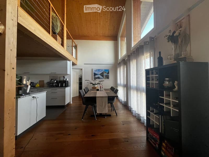 Open-plan living and dining area with wooden floors, modern kitchen, dining table with chairs, bookshelf, and decorative items.