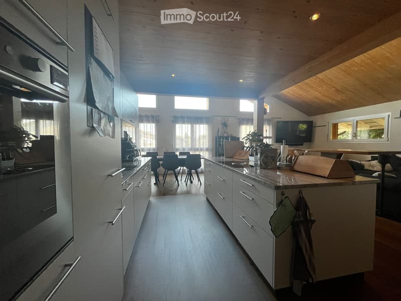 Modern kitchen with white cabinets, stainless steel appliances, island with seating, and large windows allowing natural light.