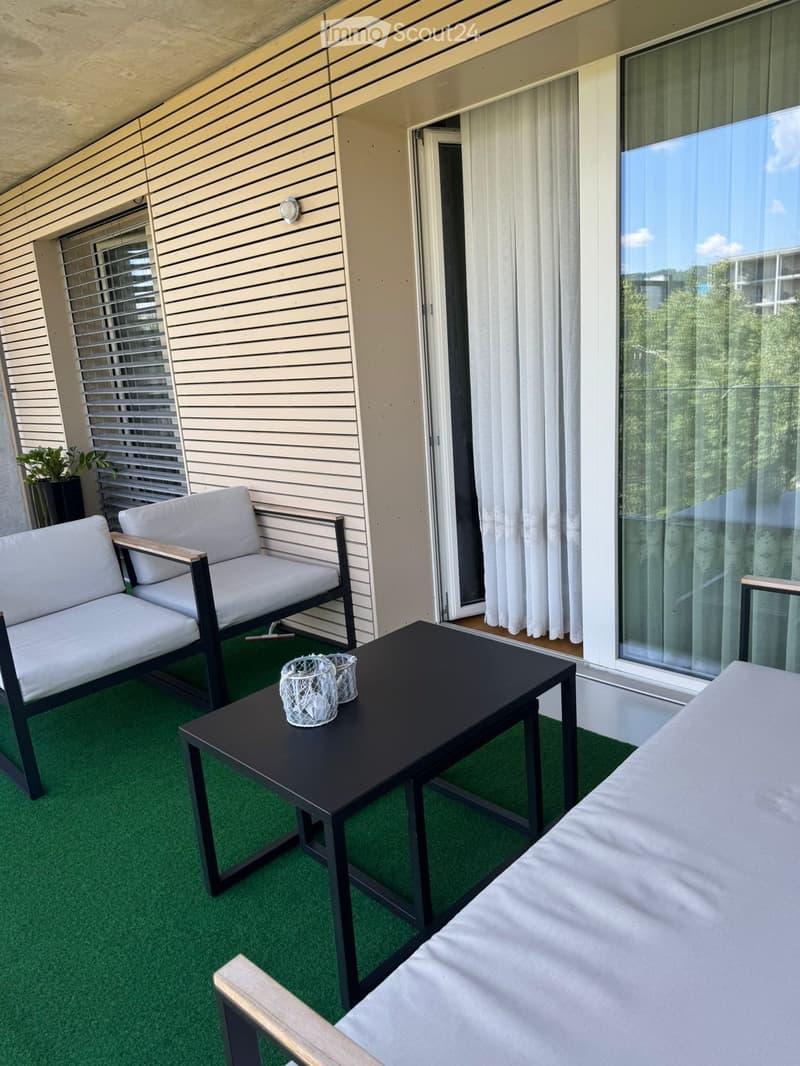 Balcony with green artificial turf, white sofa, black coffee table, and decorative items.