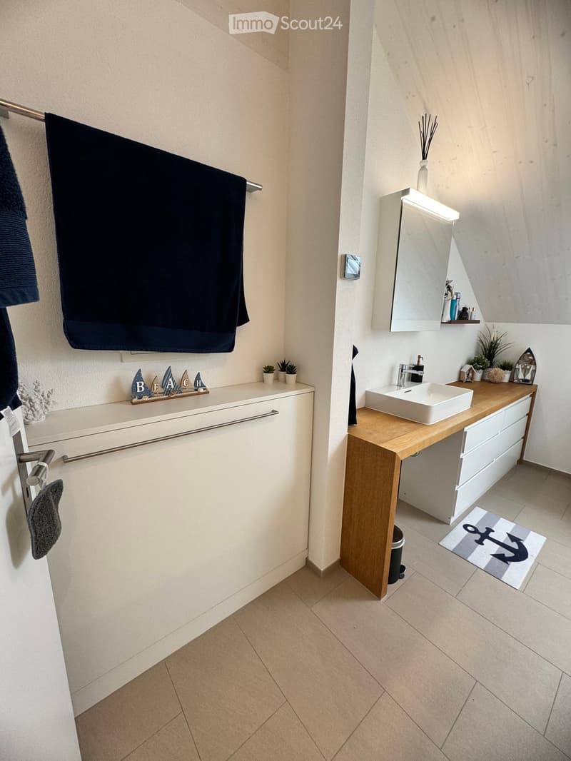 Modern bathroom with a white sink, wooden vanity, mirror, towel, and decorative items including small plants and a beach-themed sign.