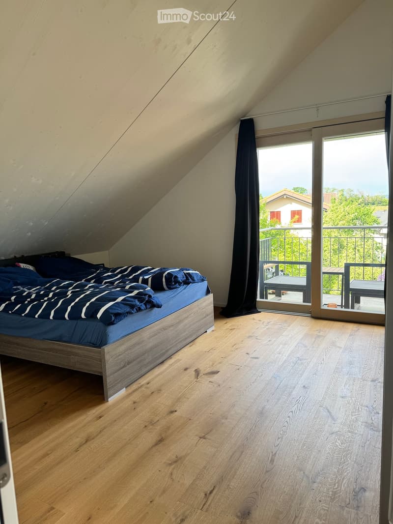 Bedroom with wooden floor, bed with blue bedding, large window with balcony access, and dark curtains.