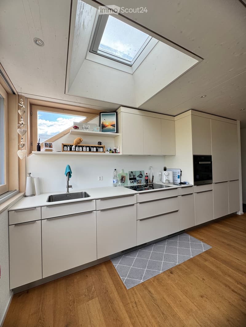 Modern kitchen with white cabinets, stainless steel sink, oven, refrigerator, coffee maker, and various small items on the counter and shelves.