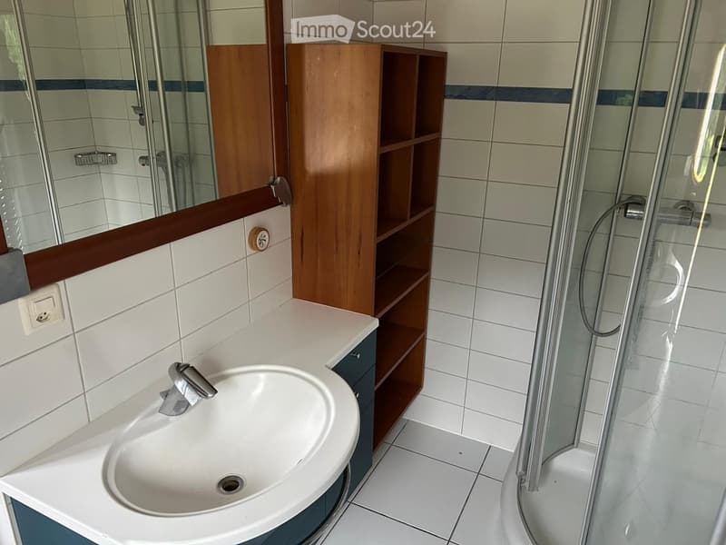 Modern bathroom with white tiles, a corner sink, a wooden shelf, and a glass-enclosed shower area.