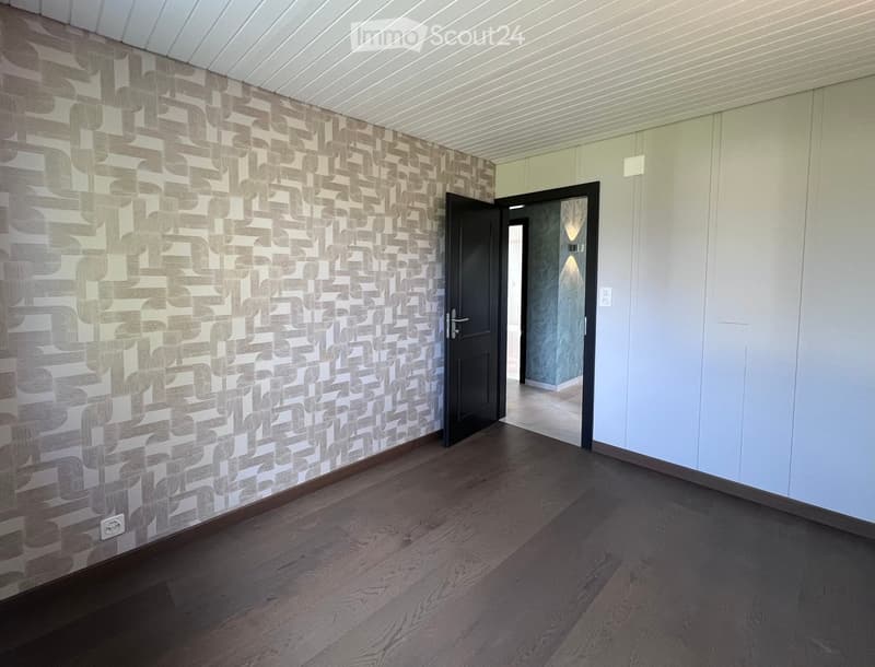 Empty hallway with wooden flooring, patterned wallpaper on one wall, and a closed door leading to another room.