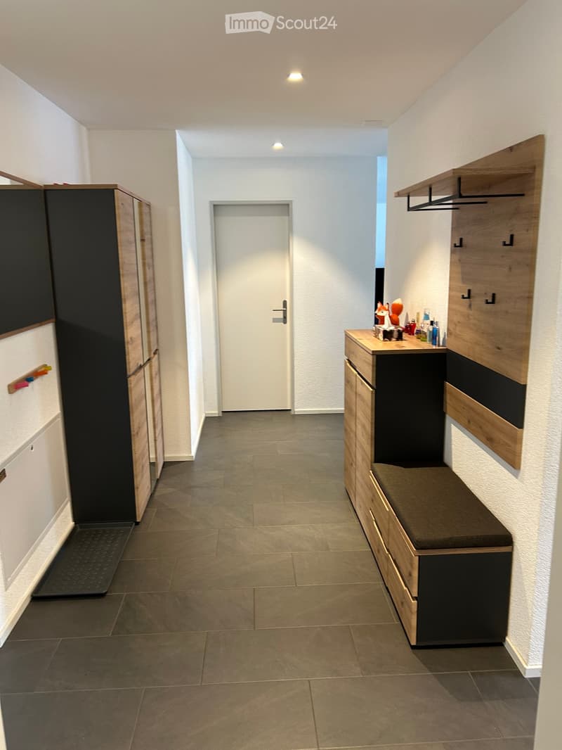 Modern hallway with tiled floor, built-in wooden bench with storage, coat rack, and small table with decorative items.