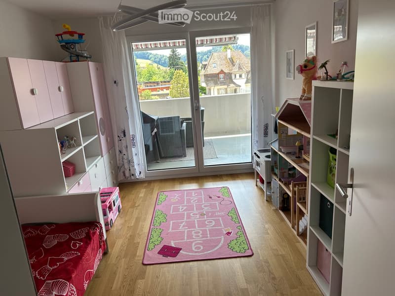 Brightly colored children's bedroom with a bed, toy car, toy horse, shelves, cabinets, play kitchen, and a hopscotch rug.