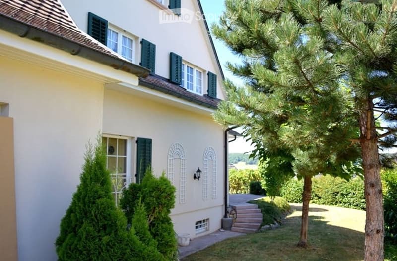 Two-story house with cream-colored exterior, green shutters, arched white decorative panels, and a small staircase leading to the entrance.