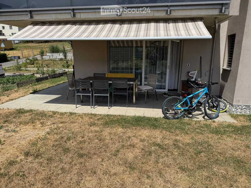 Outdoor patio area with a table, chairs, and a bicycle, attached to a house with a covered awning.