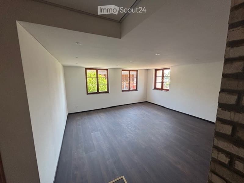 Spacious living room with white walls, large windows, and dark hardwood flooring.