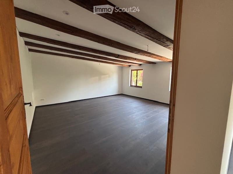 Large open space with wooden beams on the ceiling, hardwood flooring, and a single window providing natural light.